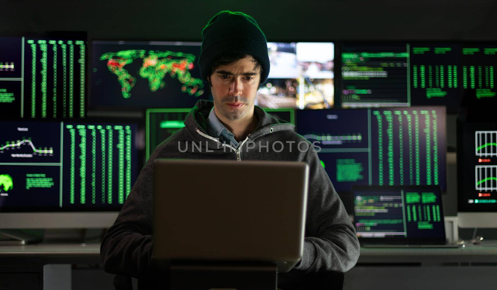 Male hacker using laptop breaks into into government data servers and infects system with virus. Multiple monitor screen background. Hacking concept.