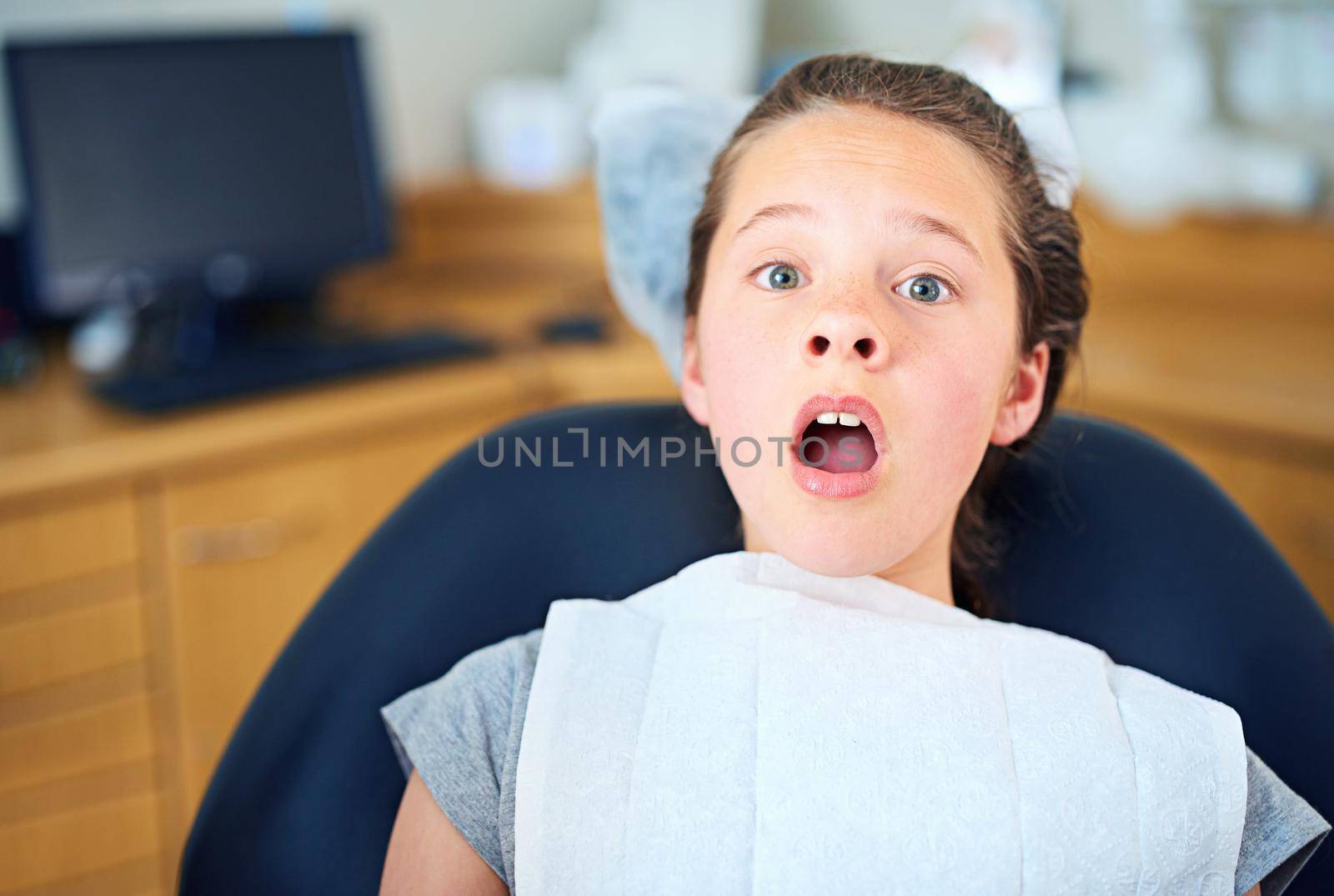 In the hot seat. Shot of a young girl looking terrified while sitting in a dentists chair. by YuriArcurs