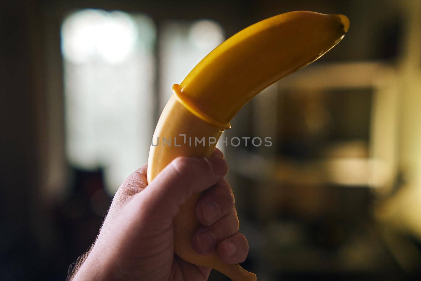 Yellow Condom and yellow banana holding a male hand indoors