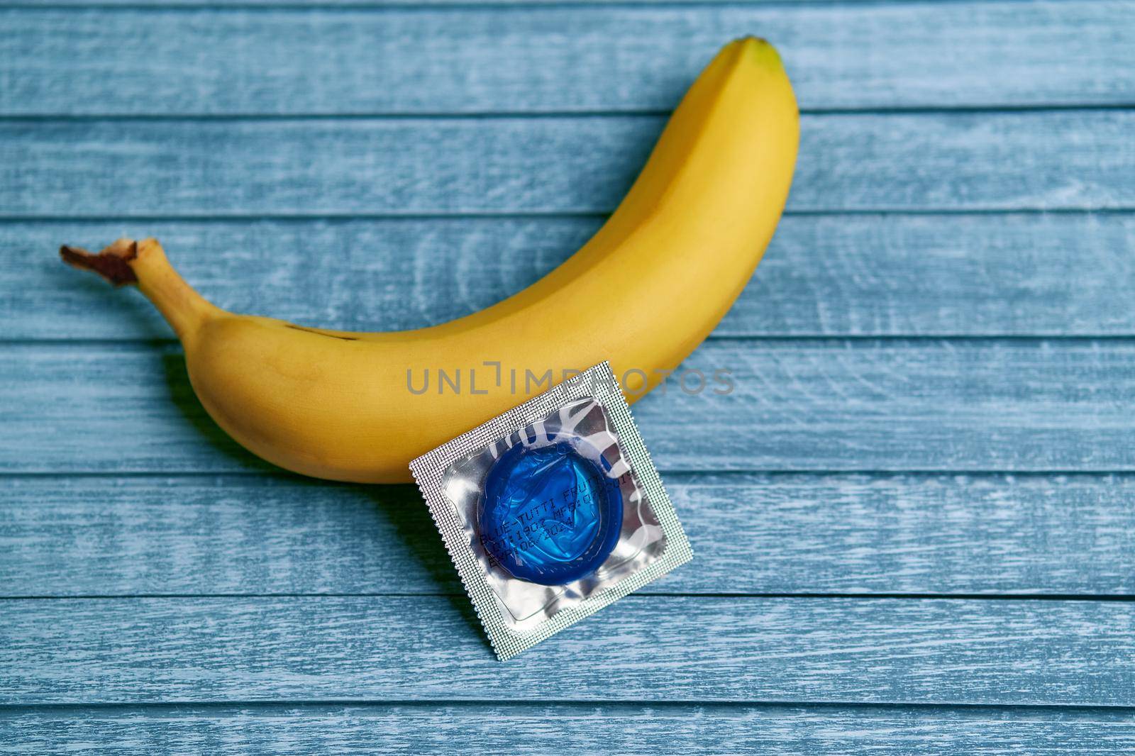 Blue Condom and yellow banana lays on a blue wooden background