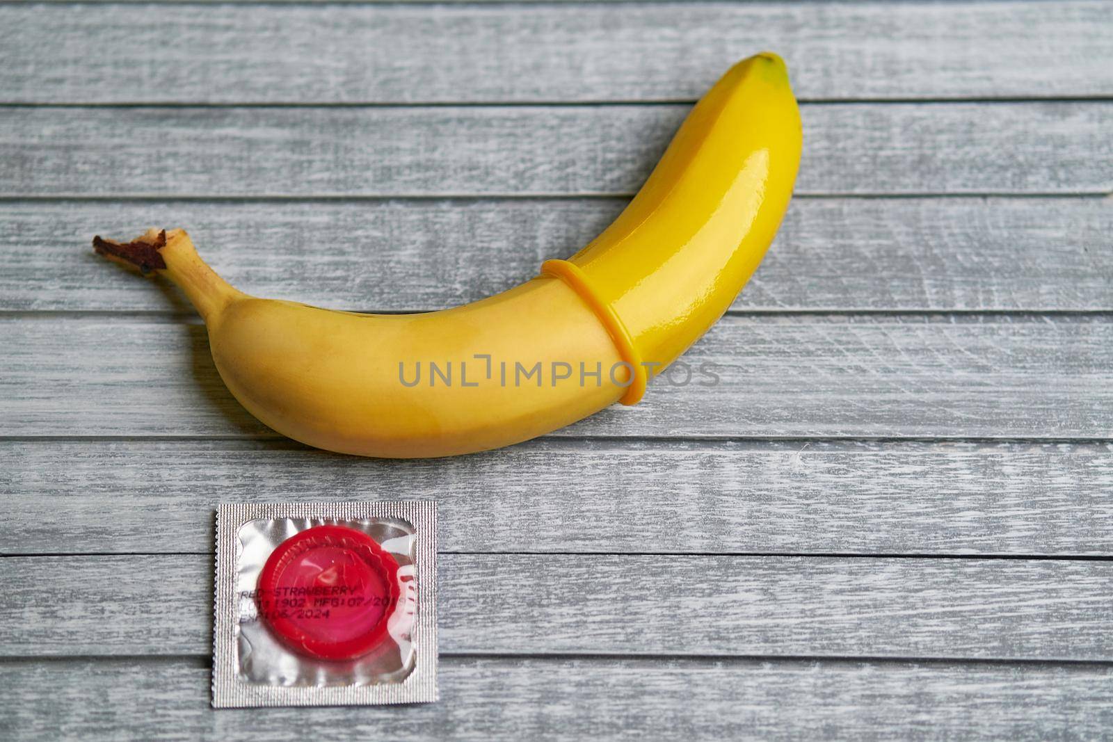 Red Condom and yellow banana lays on a gray wooden background