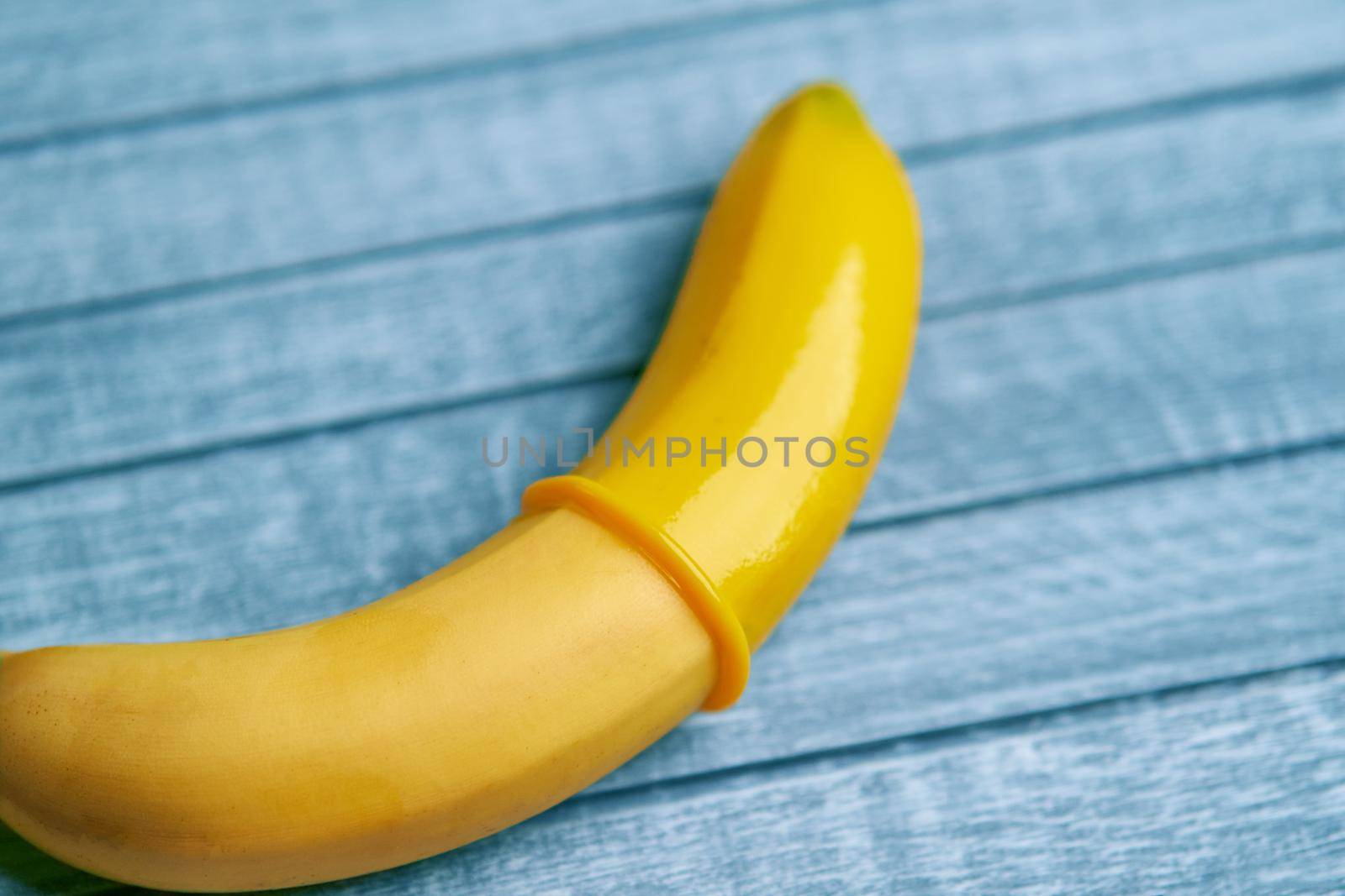 Yellow Condom and yellow banana lays on a blue wooden background