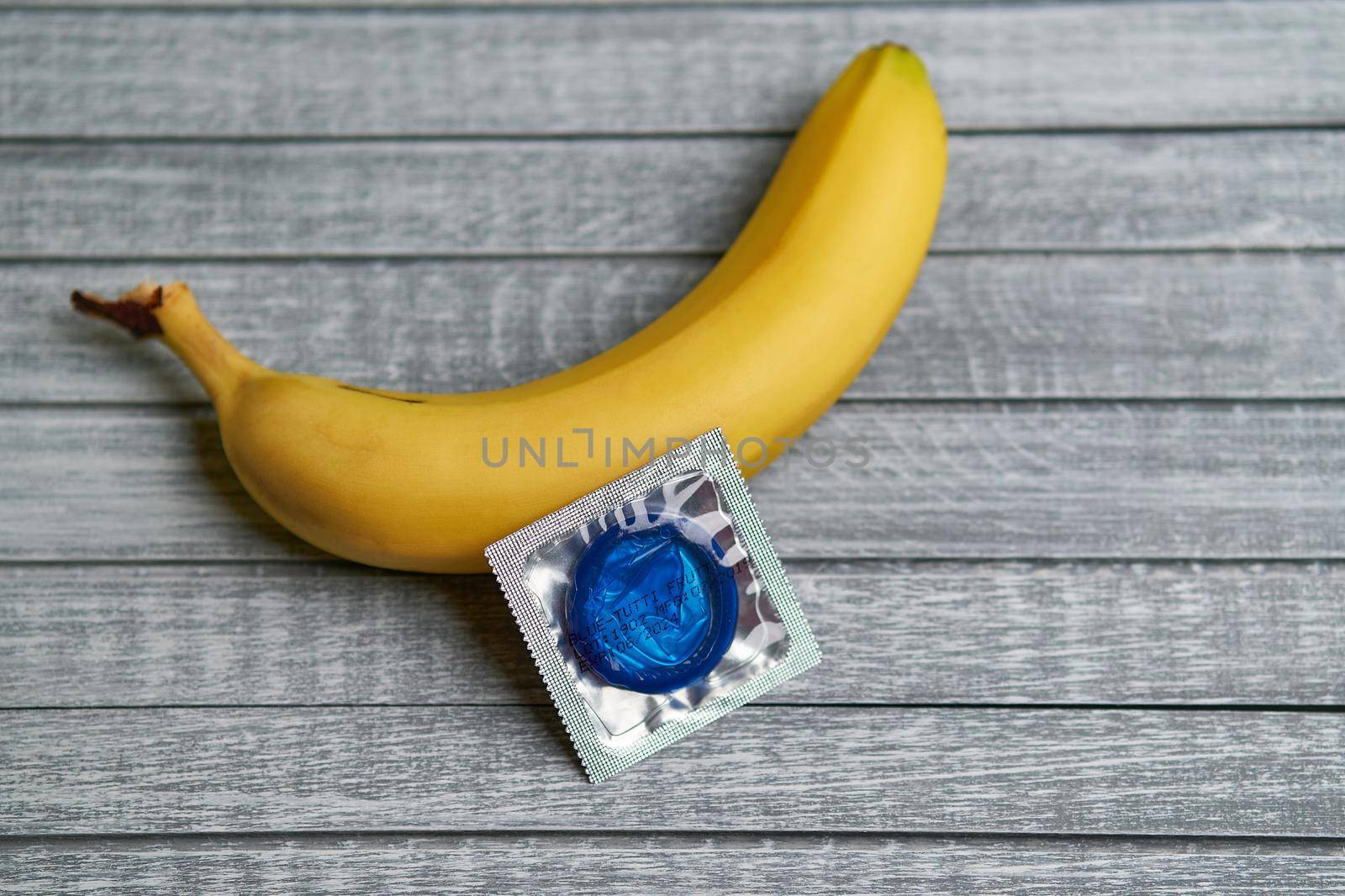 Blue Condom and yellow banana lays on a gray wooden background