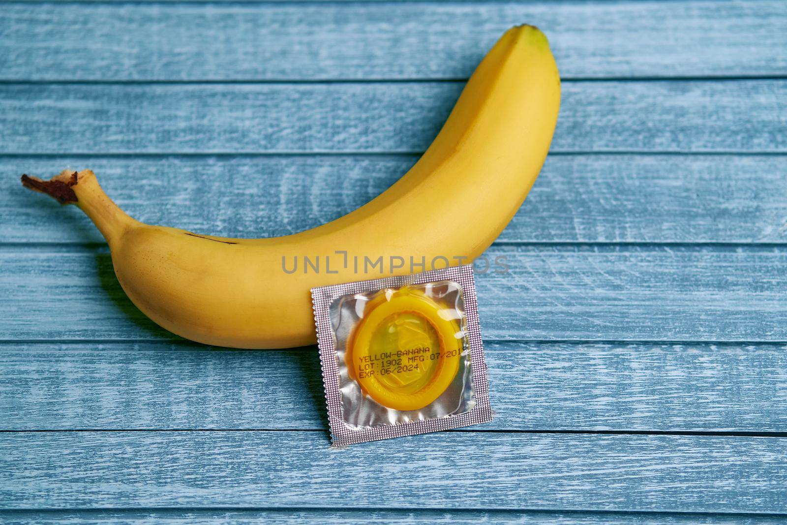 Yellow Condom and yellow banana lays on a blue wooden background