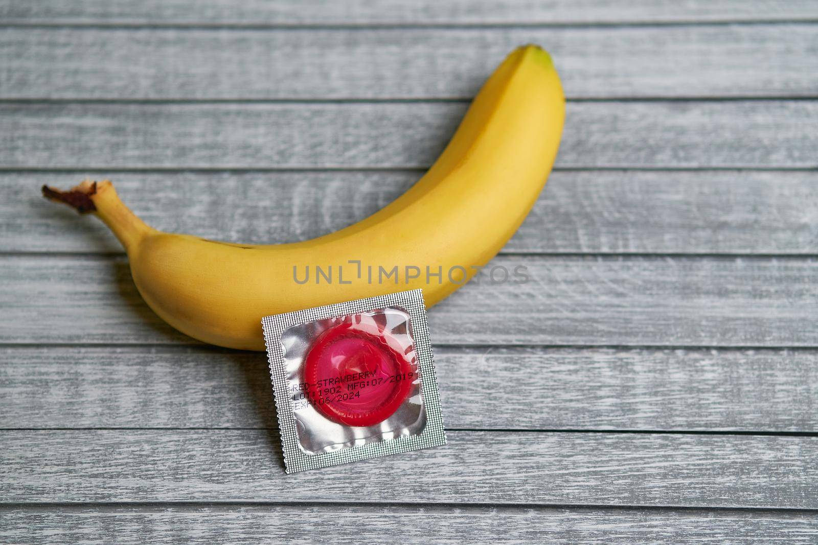 Red Condom and yellow banana lays on a gray wooden background