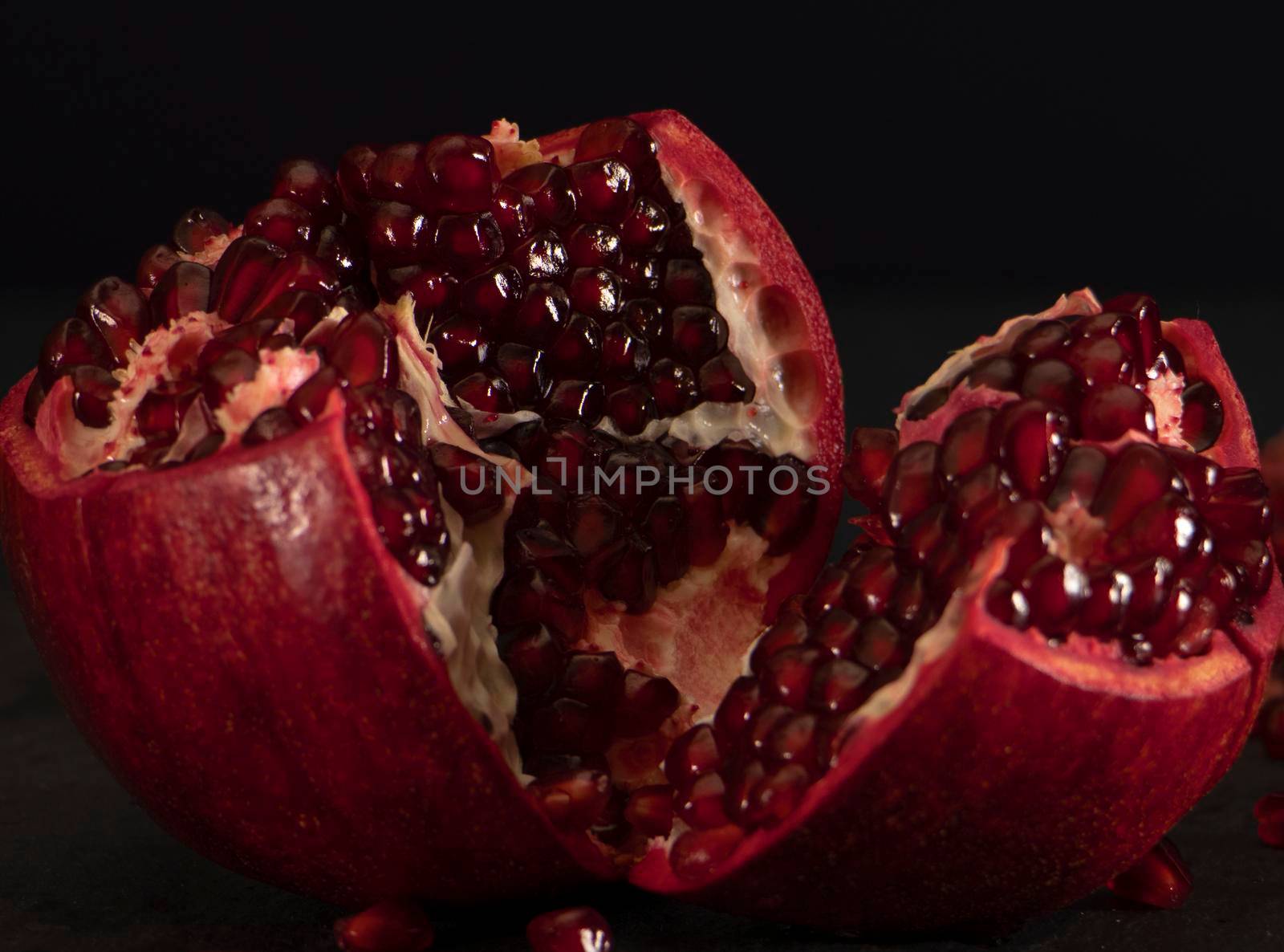 fresh open pomegranate with seeds on a black background. The red fruit is ready to eat. Peeled juicy fruit. High quality photo