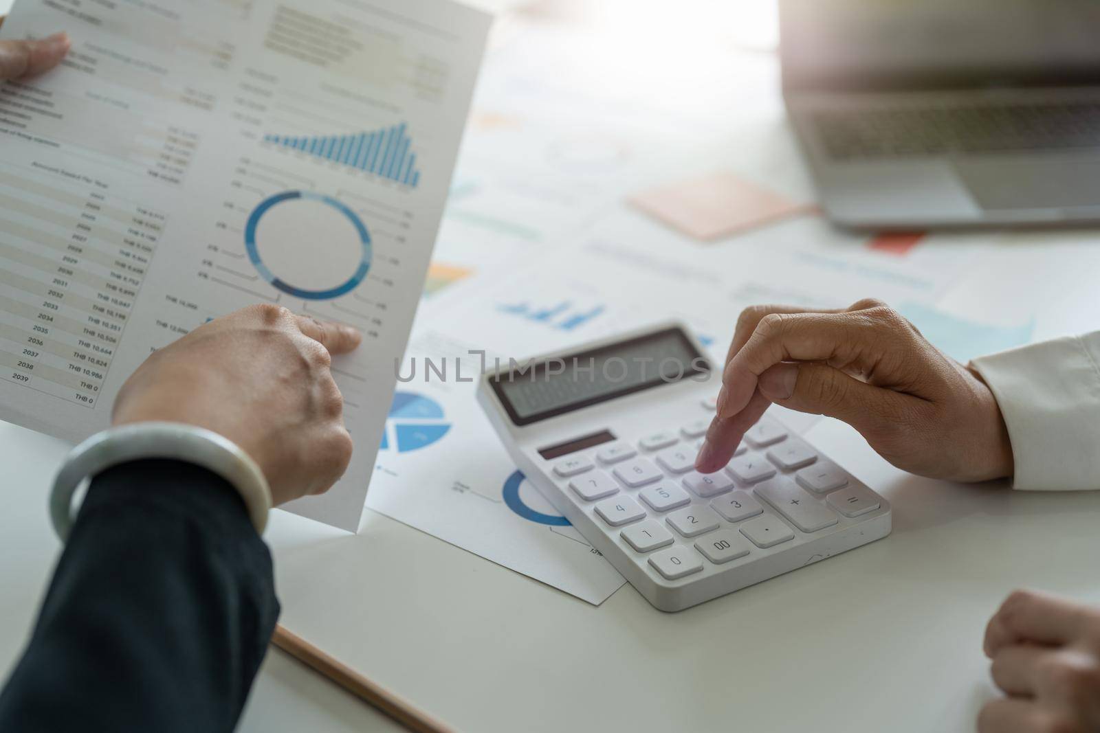 Business accounting team using a calculator and laptop computer to calculate the numbers on workplace desk in a office