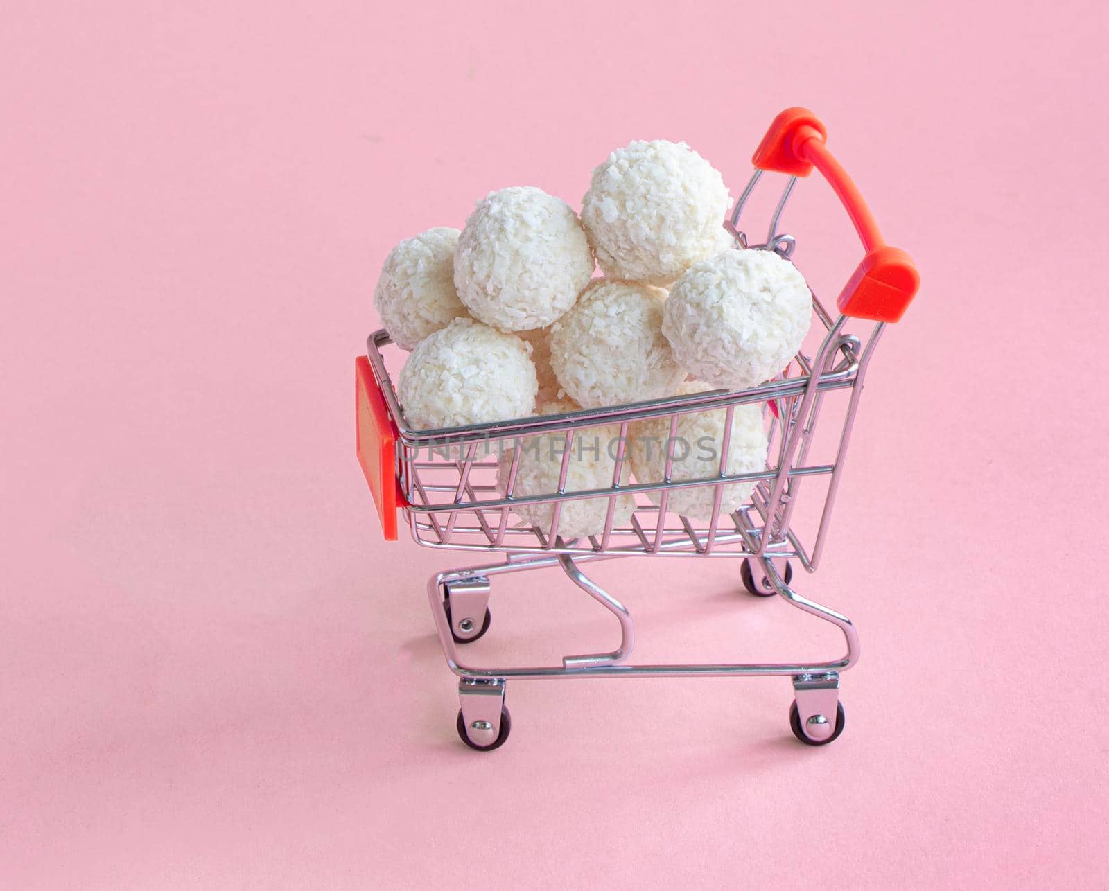 coconut round candies in a mini shopping basket, isolate on a pinc background. Supermarket shopping concept. full cart of sweets. High quality photo
