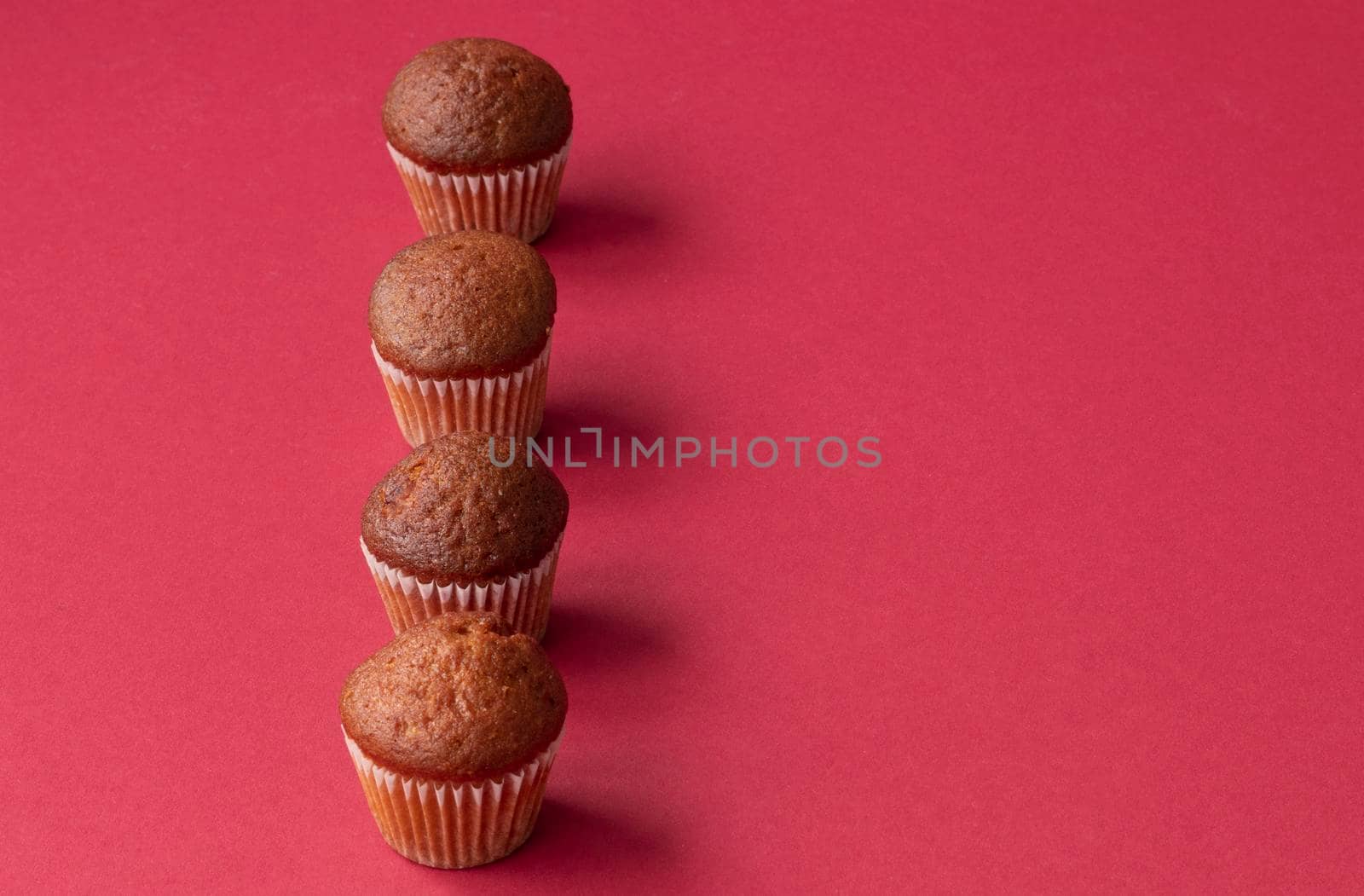 fresh mini cupcakes stand in a row on a red background. Muffins in paper forms. Confectionery background concept. Place for text. High quality photo