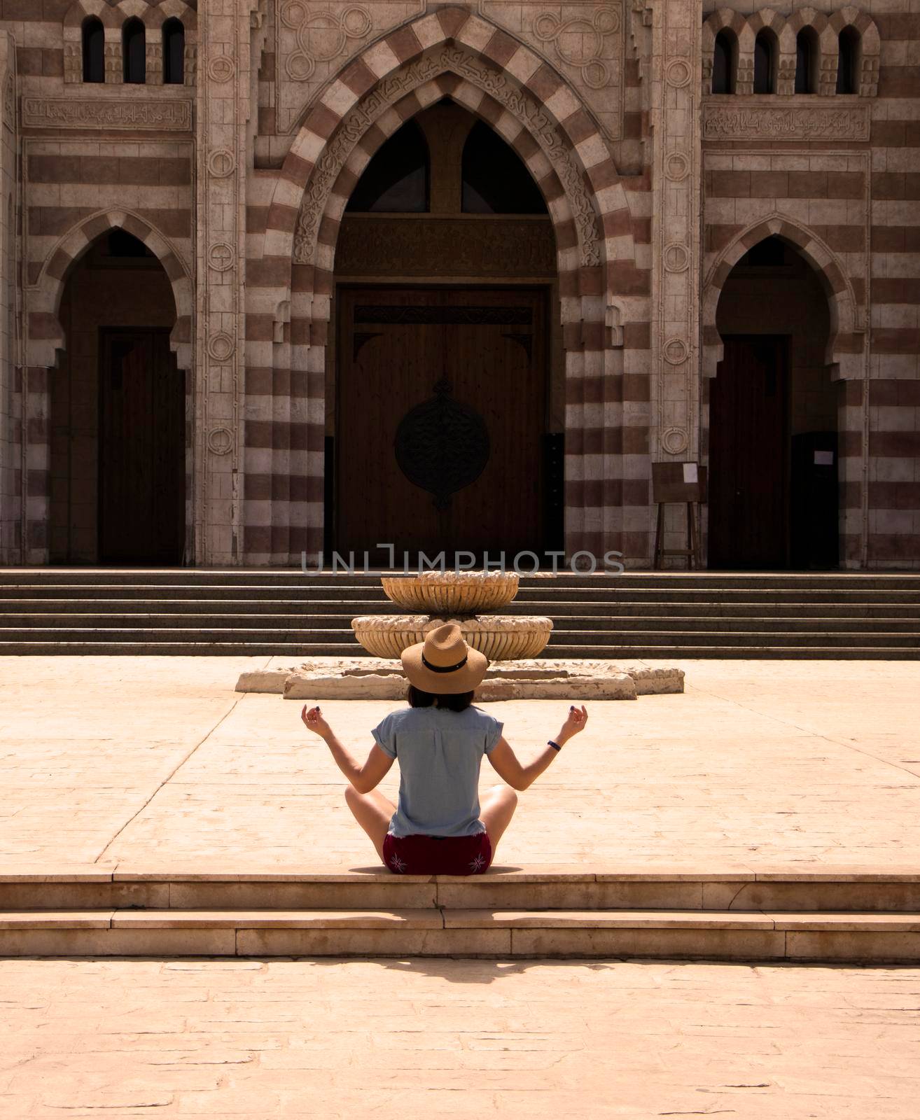a girl in a straw hat sits with her back in a meditate pose before entering the temple. High quality photo. Yoga Concept. Hand Woman Practicing Lotus Pose