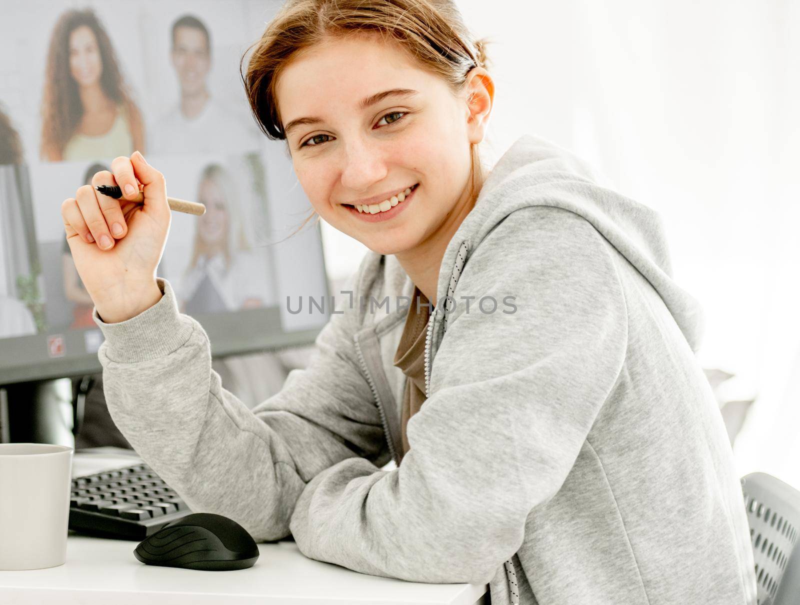 Girl during remote educaton class via video link with friends classmates on display. Teenager e-learning on distance with computer at home in coronavirus pandemic time