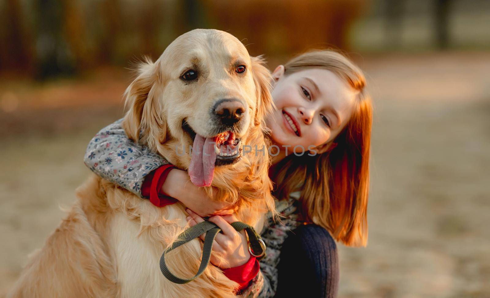 Preteen girl with golden retriever dog sitting in park in beautiful spring autumn day. Adorable female child kid hugging doggy pet outdoors and smiling portrait