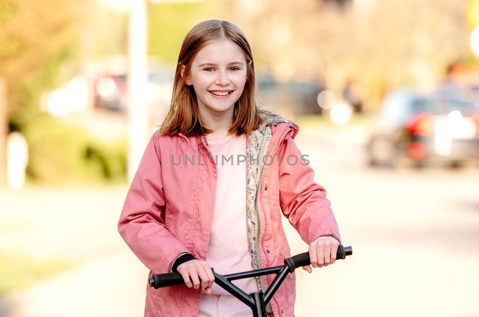 Funny little girl rides a kick scooter on a street near home