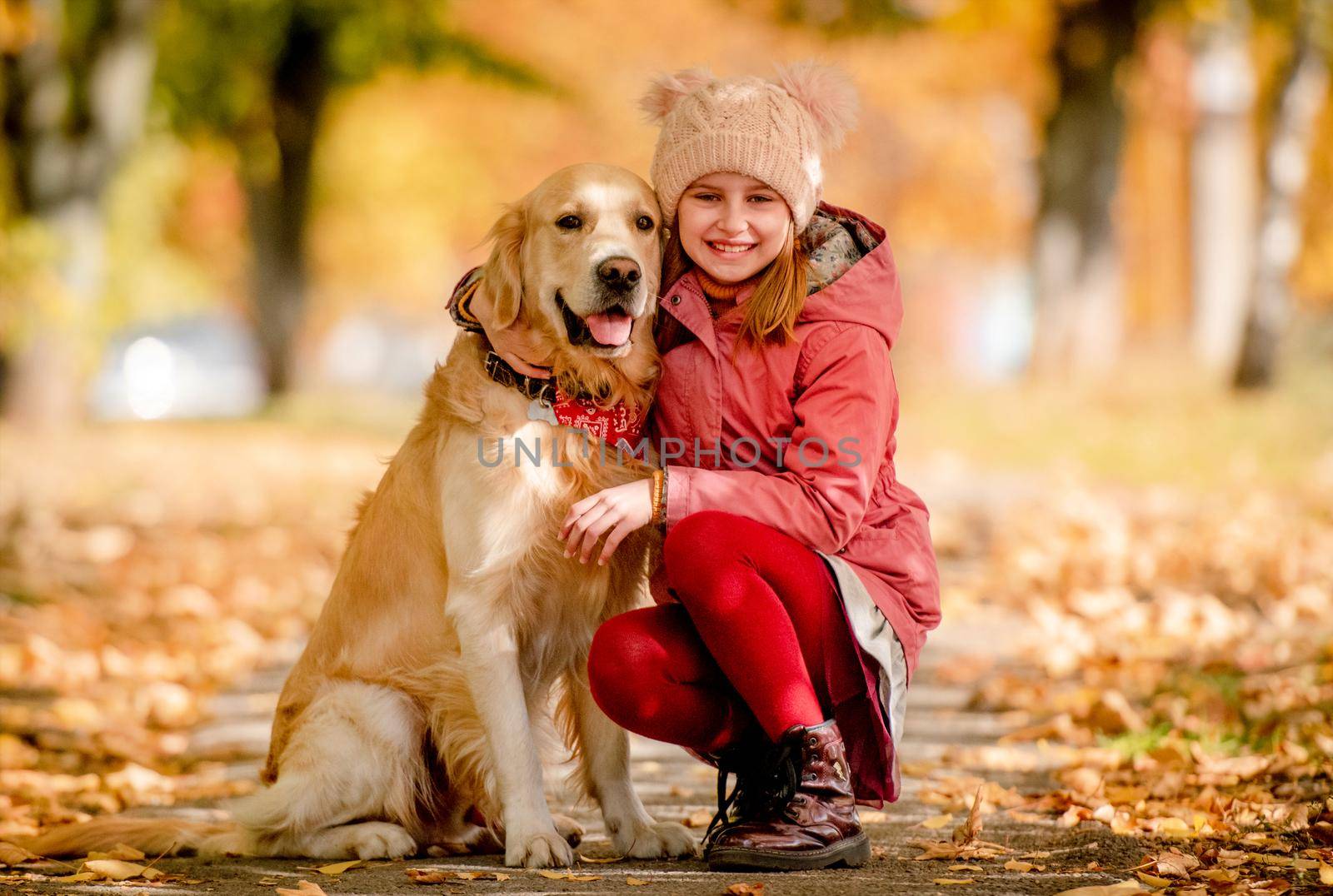 Preteen girl kid with golden retriever dog sitting at autumn park and hugging doggy. Beautiful portrait of child and pet outdoors at nature
