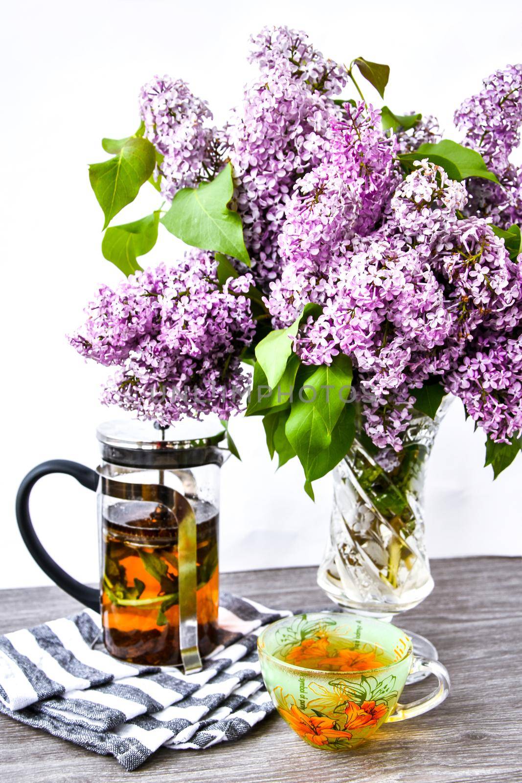fresh herbal tea cup, teapot and blossom Violet lilac flowers bouquet in glass vase, Kitchen interior decorations. Mother's day congratulation,