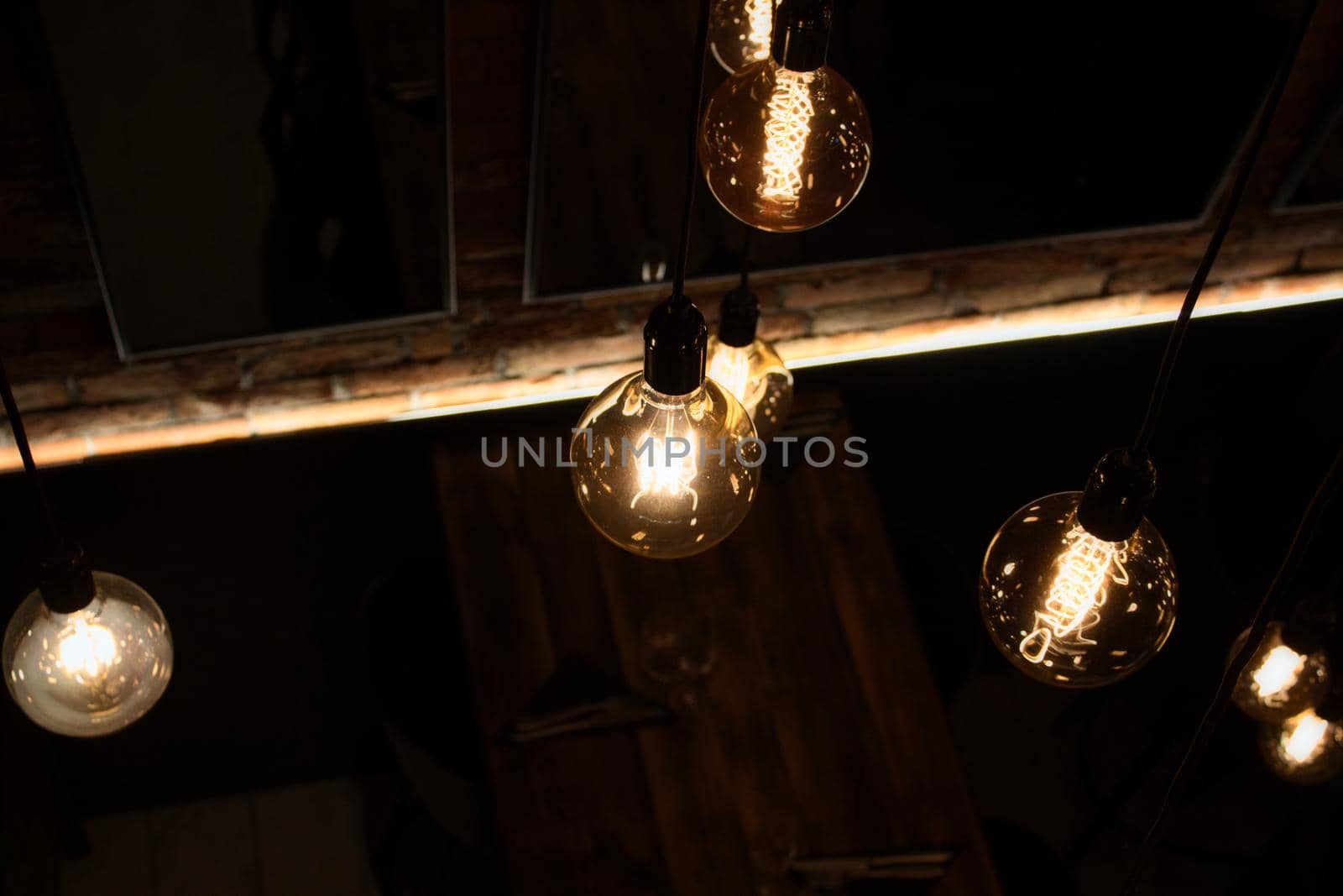 Warm glowing glass light bulbs hanging from the ceiling of a modern restaurant by tennesseewitney