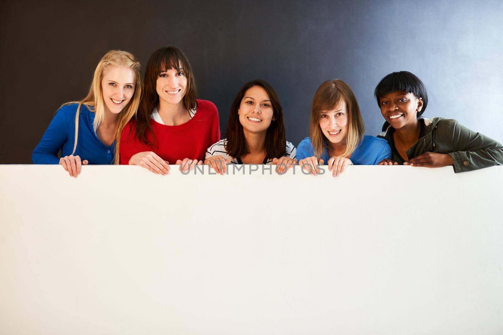 Place your message here. Shot of a group of women holding a blank sign against a dark background. by YuriArcurs