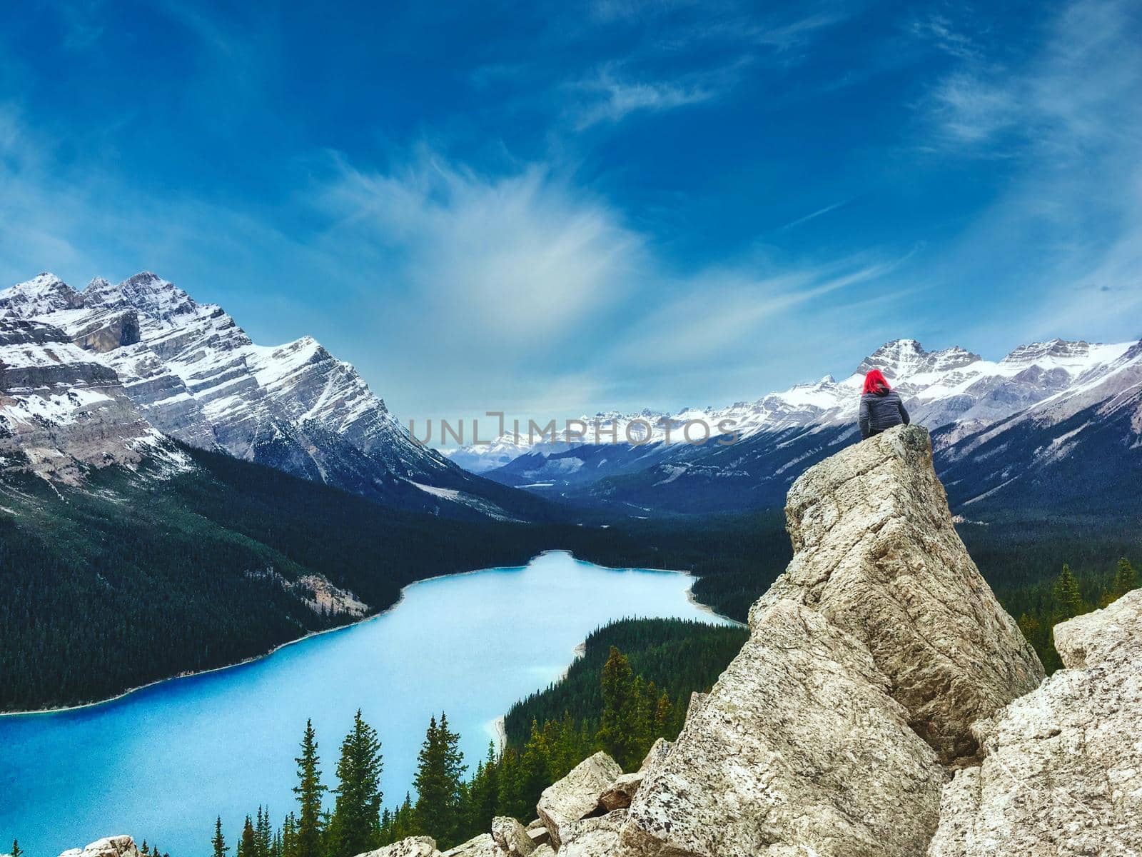 Peyto Lake, Banff National park in Canada with the Canadian Rockies in the distance, and a woman sat on a rock in the foreground with pink hair by tennesseewitney