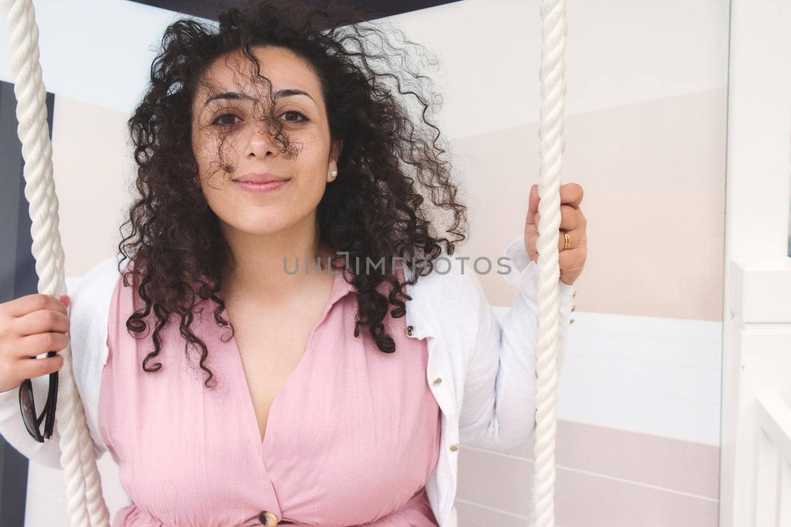 Beautiful young woman with curly hair on a swing looking at the camera