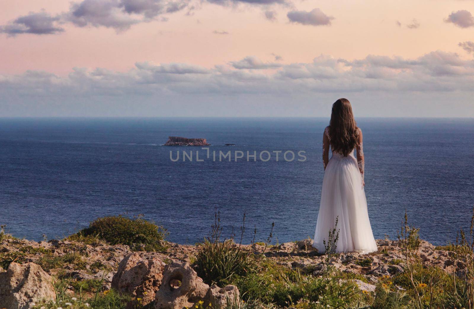 A bride in a white wedding dress standing on a cliff edge looking out to sea