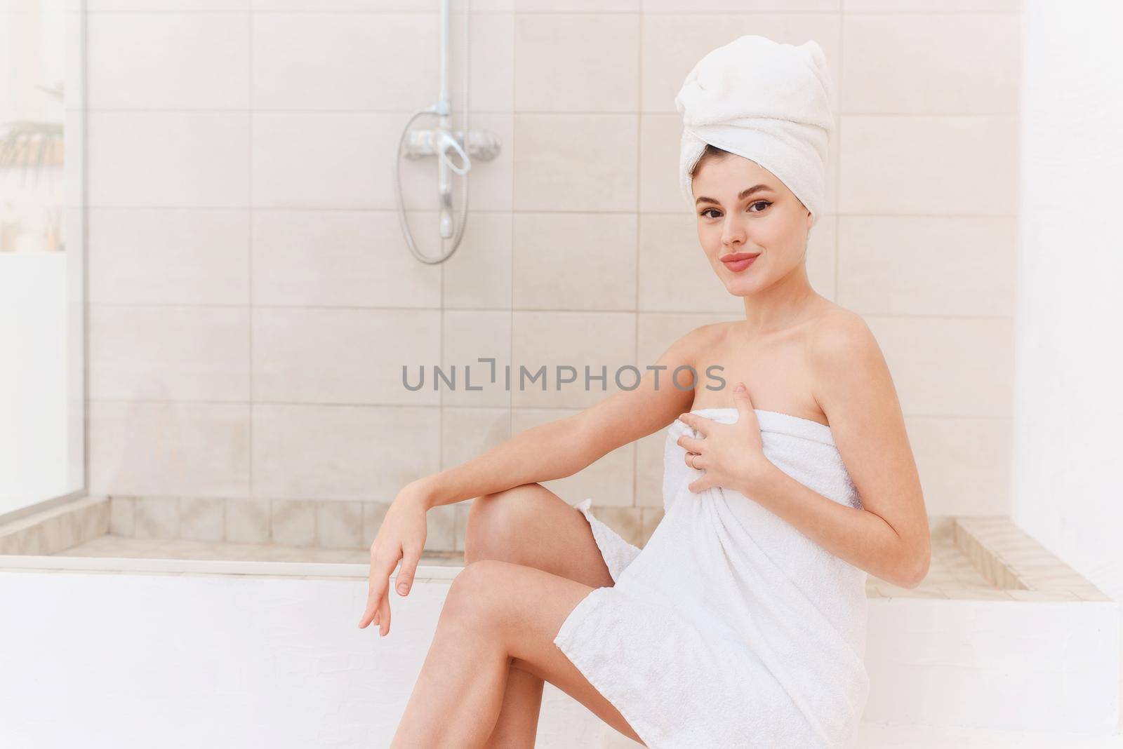 A young smiling woman takes care of her skin and hair after a shower. Spa treatments at home, skin care