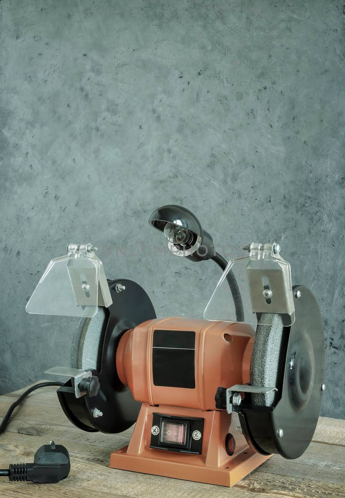 A small electric tool sharpening machine with two grinding wheels, protective casings, protective screens and a lamp. Front view, copy space.