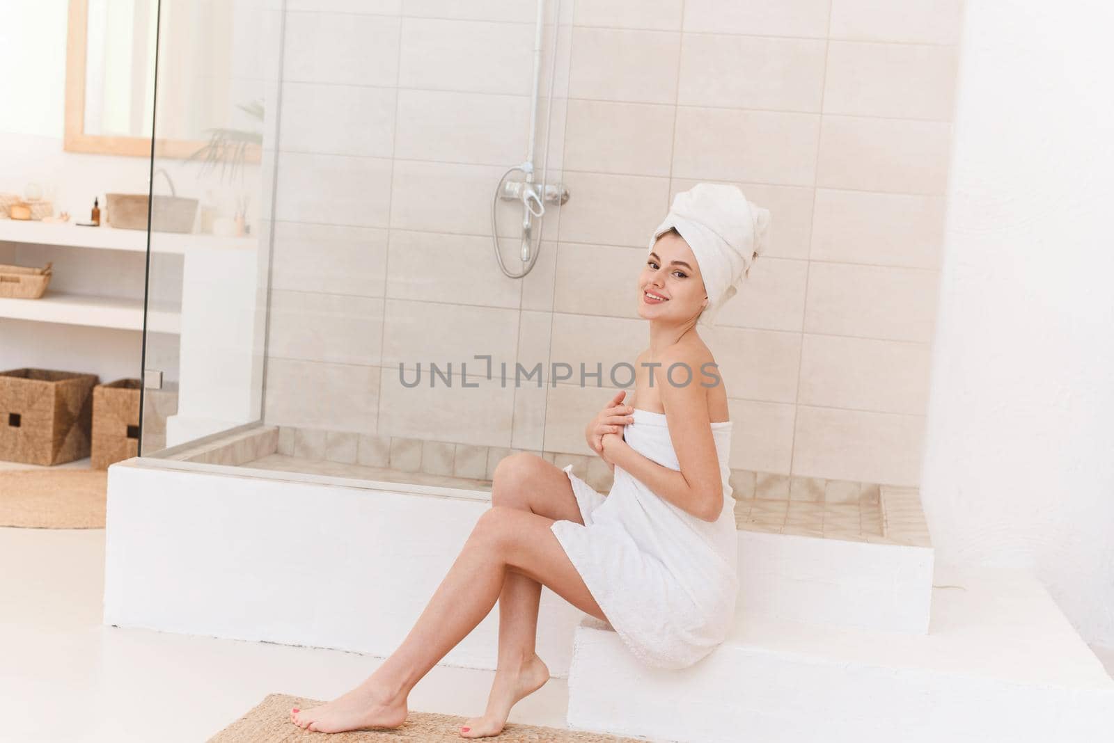 Relaxed young caucasian model wears towel wrapped on head and body, feels refreshed after shower, has healthy clean soft skin, poses in cozy trendy bathroom. Women, beauty and hygiene concept