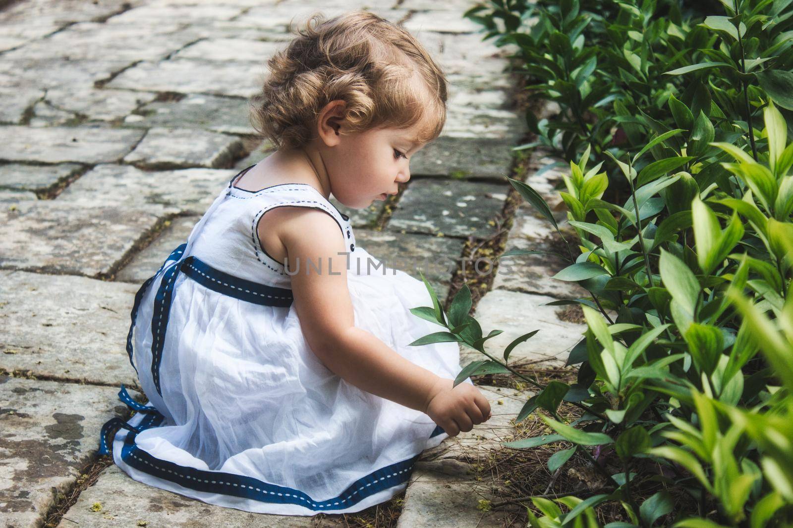 A beautiful cute young girl playing on a garden path with green leaf foliage