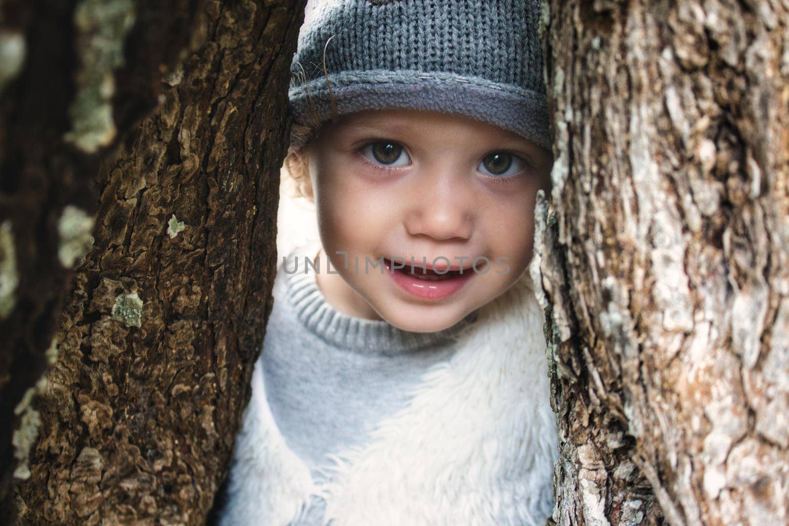 Close up of beautiful young girl model smiling and peering through a gap between tree trunks in the woods wearing winter clothes