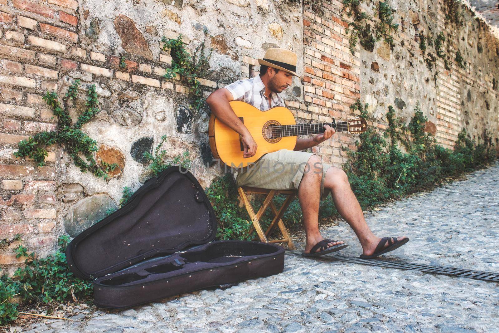 Granada / Spain - August 21 2019: A male busker sitting playing the Spanish acoustic guitar in an alleyway by tennesseewitney