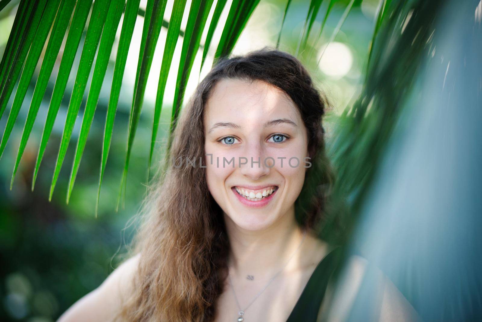 Young beautiful natural cheerful woman with healthy face and skin in exotic greenery. Closeup fresh face of attractive girl. Summer model. Natural beauty concept.