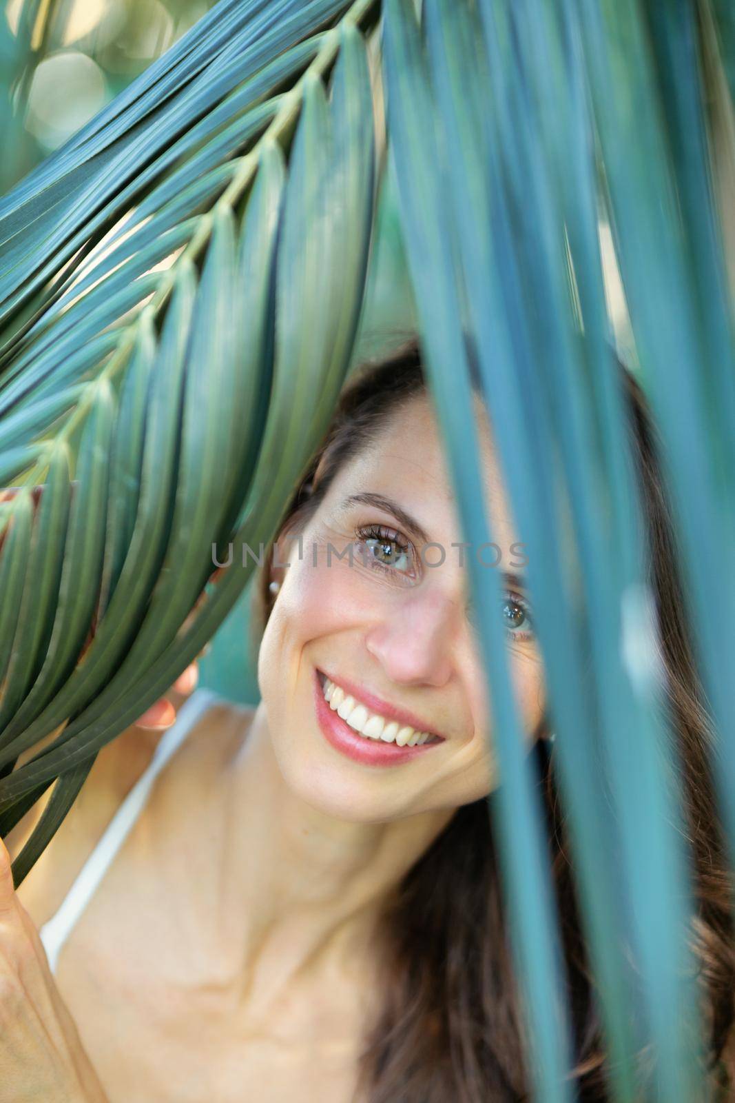 Young beautiful natural cheerful woman with healthy face and skin in exotic greenery. Closeup fresh face of attractive girl. Summer model. Natural beauty concept.