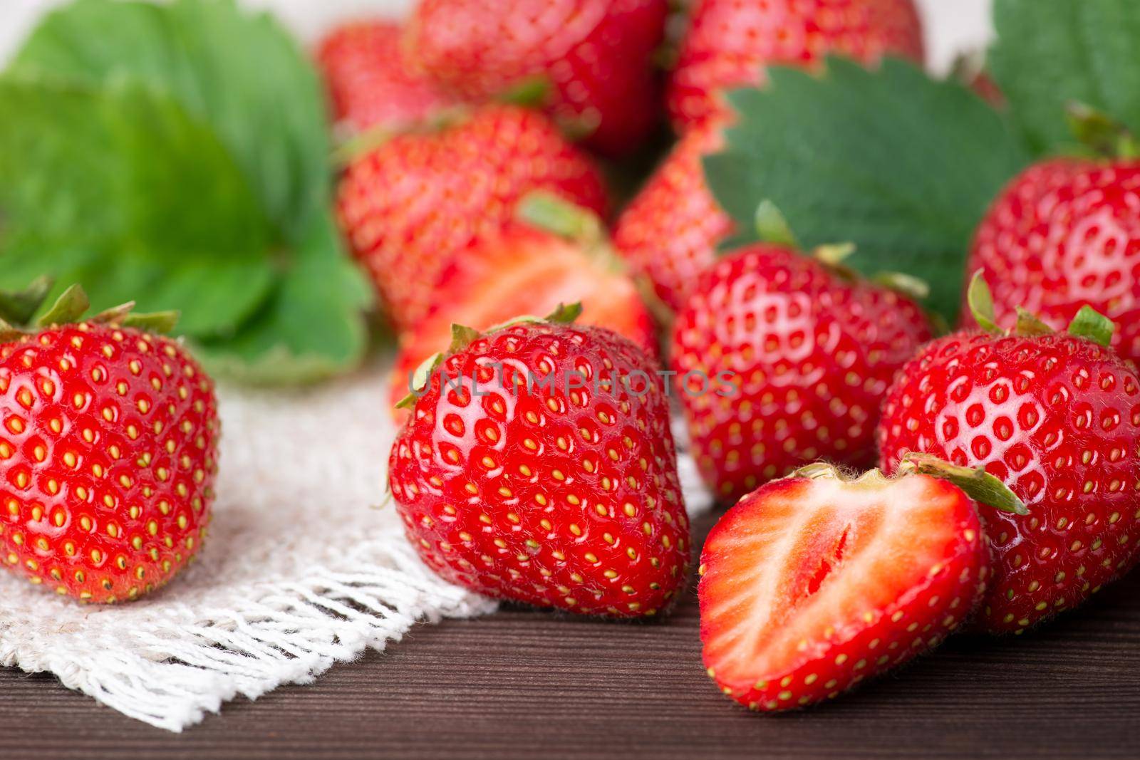 Tasty fresh strawberries on a white linen kitchen towel with some leaves in the background