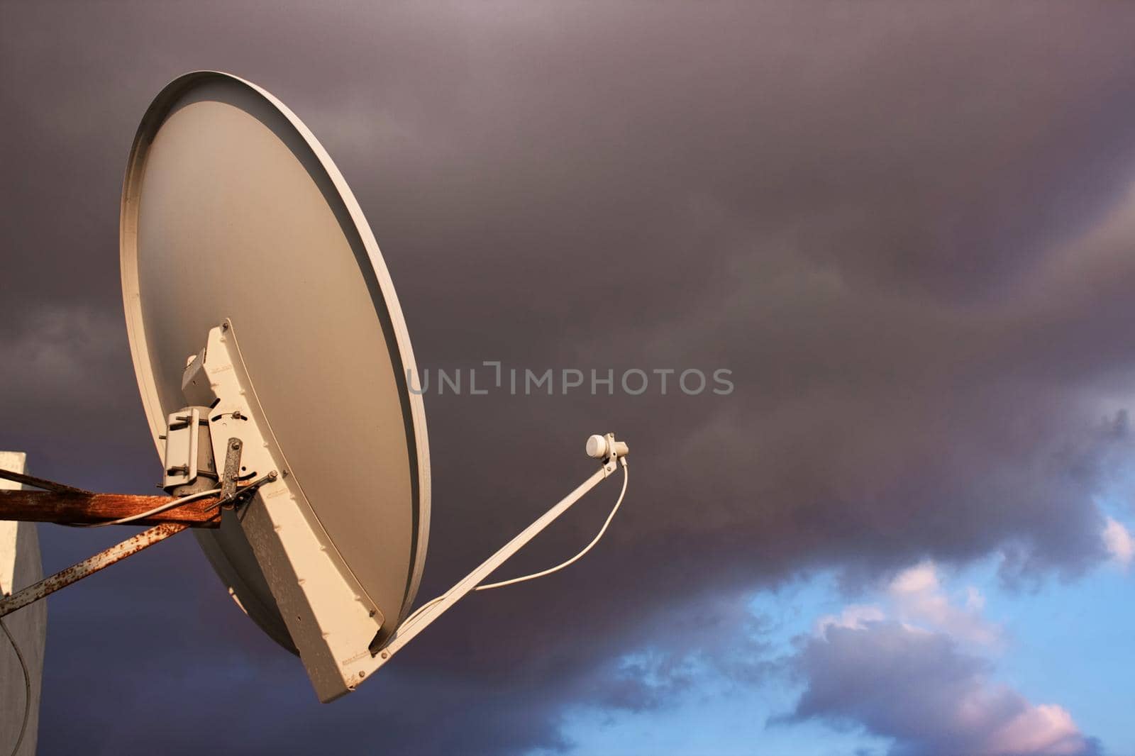 Satellite dish on a rooftop against a cloudy moody sky background by tennesseewitney