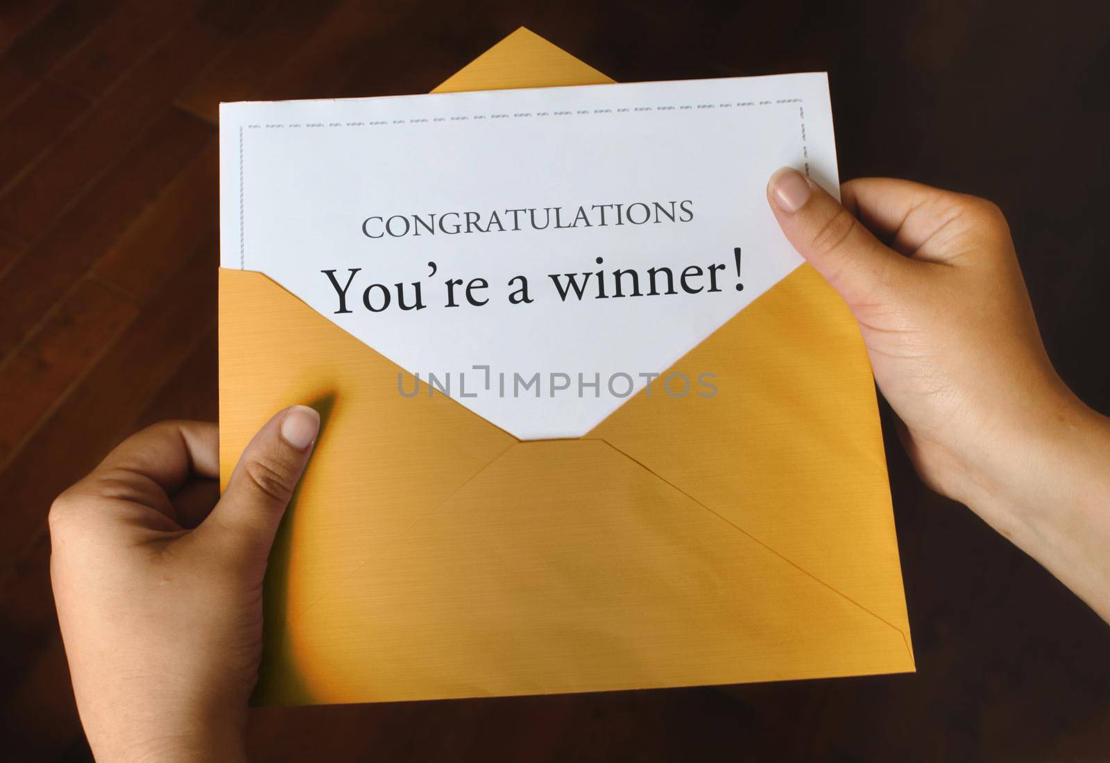 An open shiny gold envelope with a letter that says Congratulations You're a winner! with female hands holding it up
