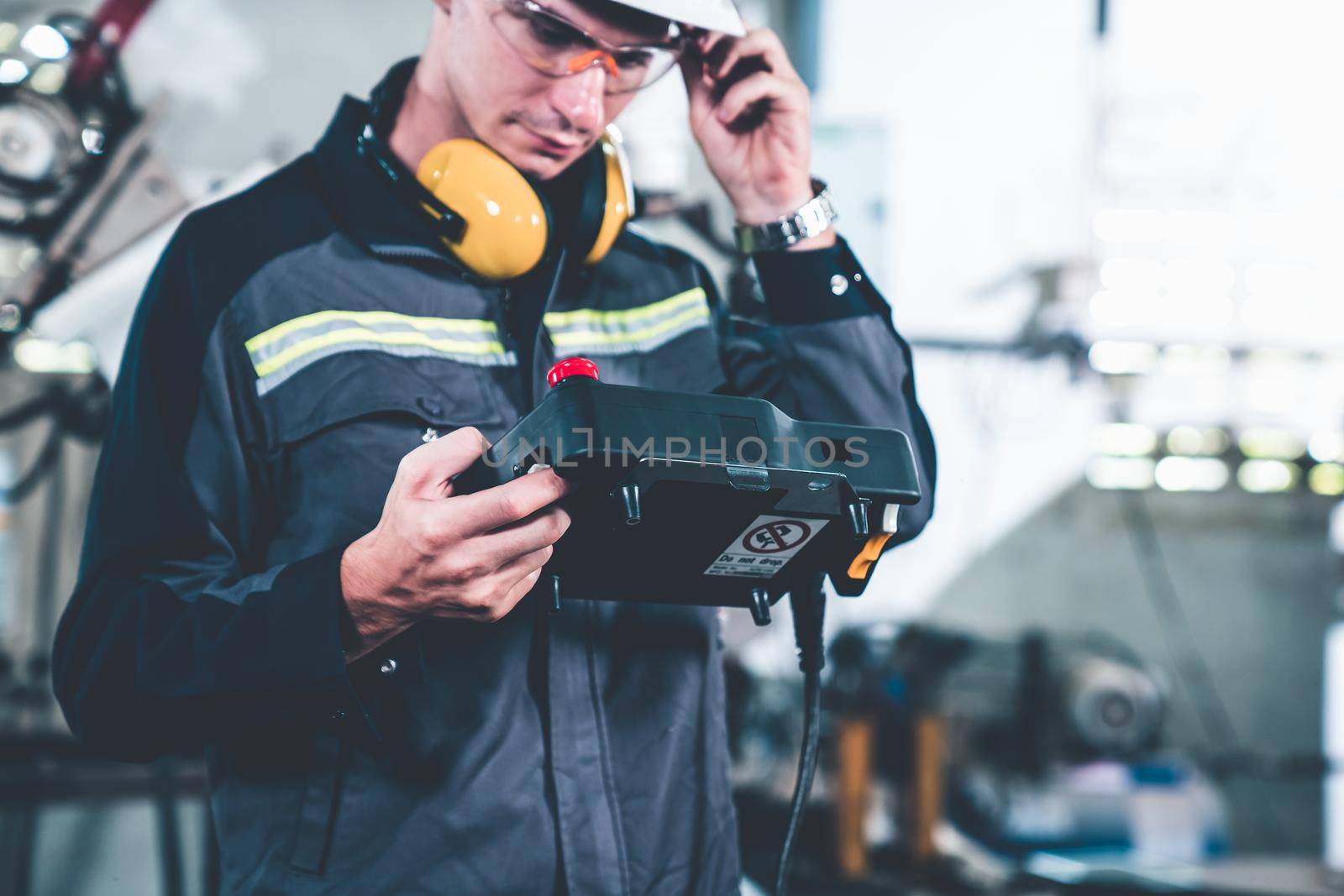 Young factory worker working with adept robotic arm in a workshop . Industry robot programming software for automated manufacturing technology .