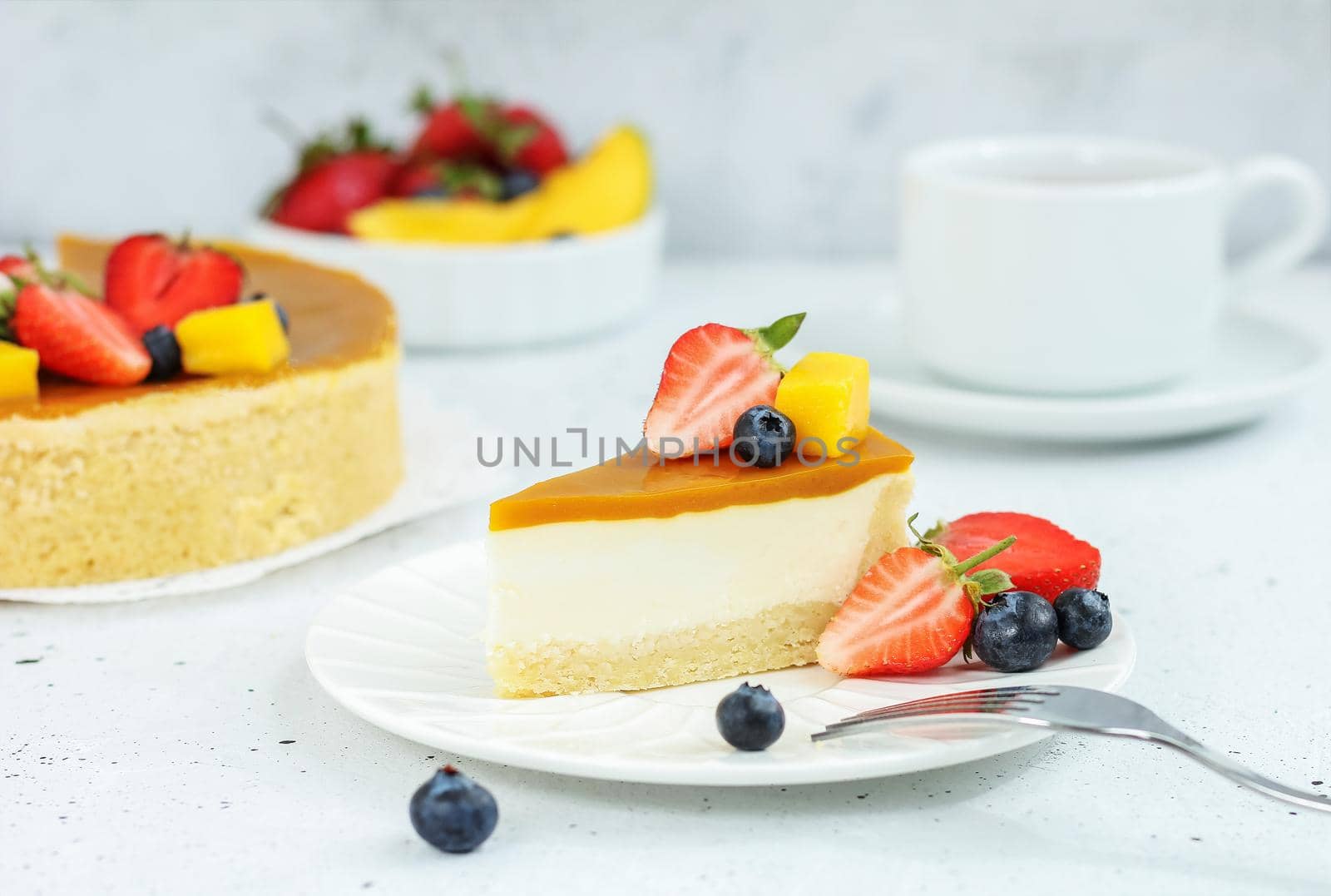 A piece of cheesecake with mango on a plate with a tea fork decorated with berries and flowers on a gray background. Healthy food. by lara29