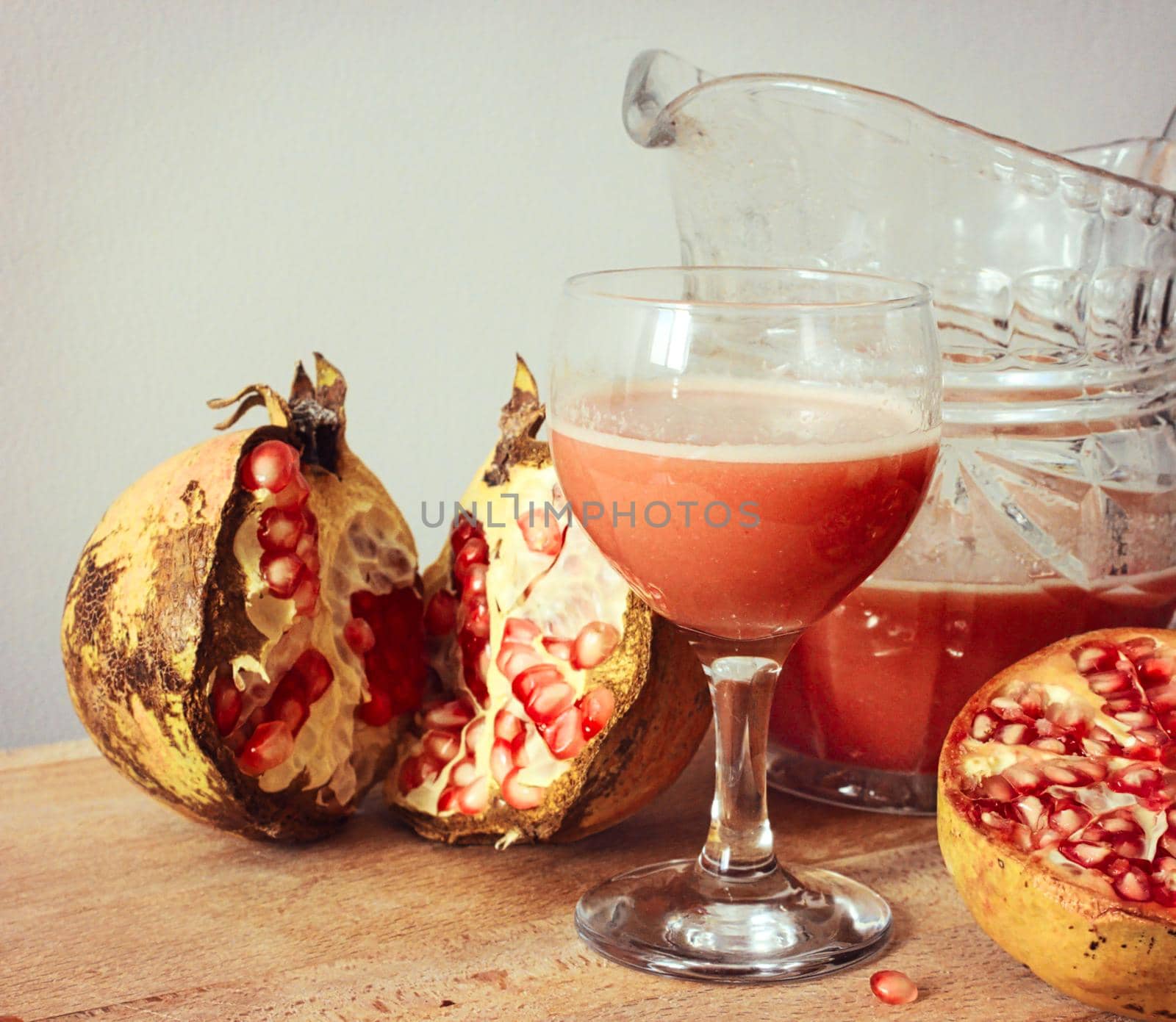 Fresh pomegranate juice in a glass jug with sliced pomegranates on a chopping board