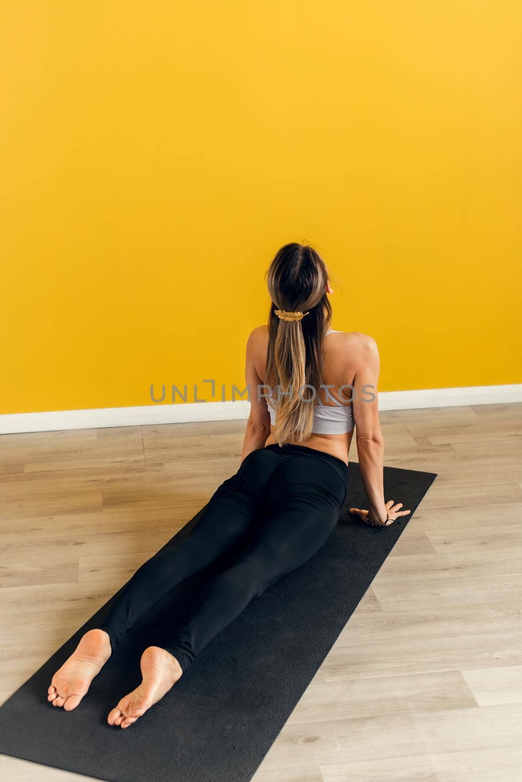 Side view of a beautiful young woman in sportswear practicing yoga on an exercise mat on a yellow background. Stretching the muscles of the back and legs, yoga.