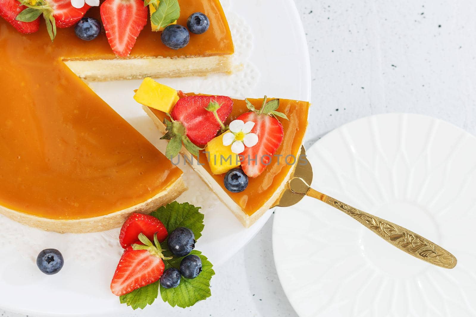 A piece of sliced mango cheesecake on a stand, garnished with berries and flowers. Healthy dessert. Vegetarian food Copy space. by lara29