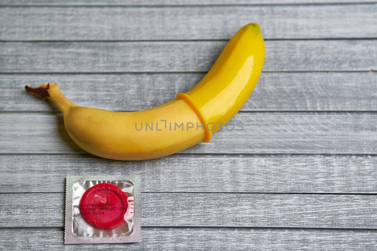 Red Condom and yellow banana lays on a gray wooden background