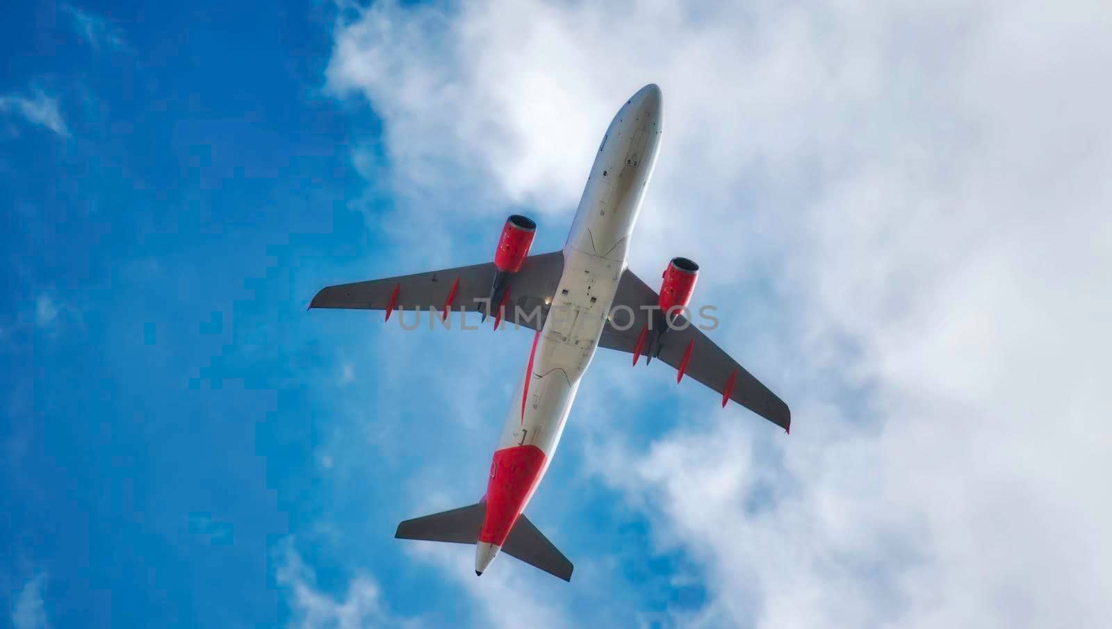 Underbelly of a jet airplane flying in the air isolated against a blue sky with clouds