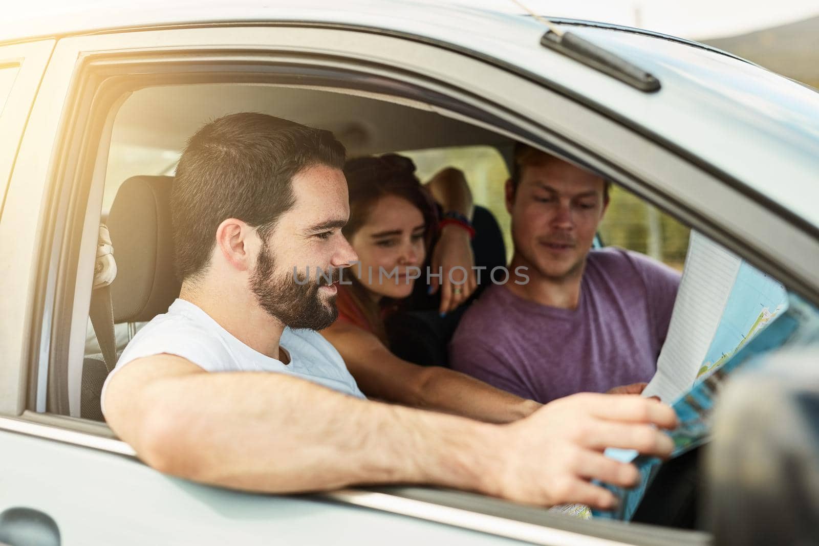 All systems go. Shot of a group of young friends getting ready to drive to their destination in their vehicle while looking at a map. by YuriArcurs