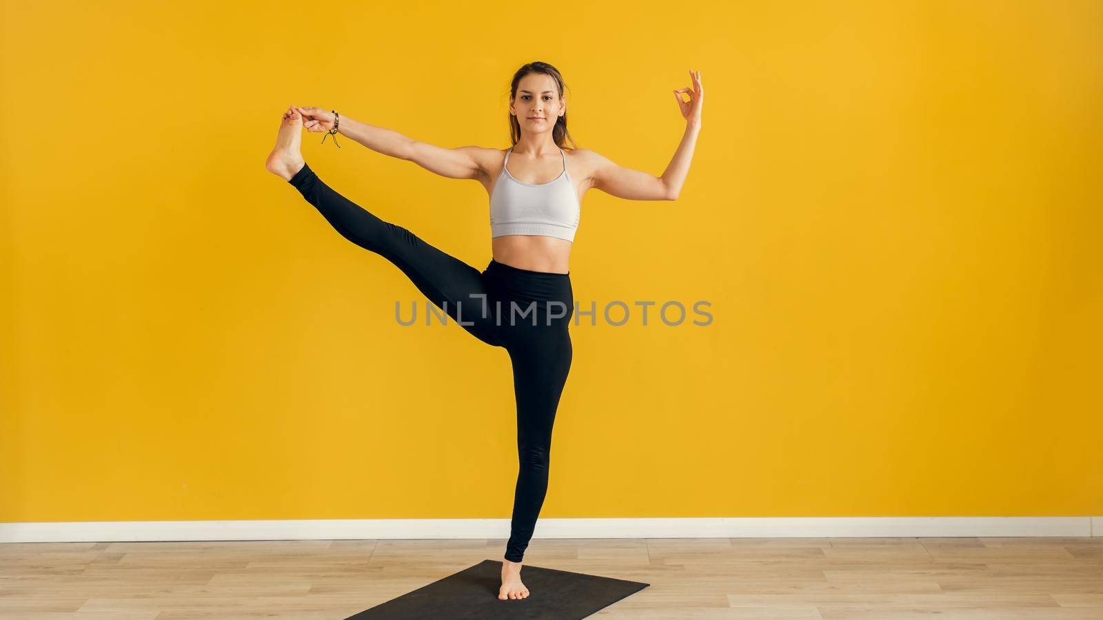 Beautiful young woman practicing yoga indoors. Utthita Hasta Padangusthasana, Extended Hand to Big Toe pose. Yellow background. Web banner.