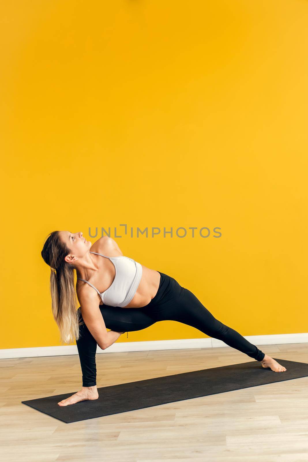 Beautiful female trainer is engaged in pilates workout and hatha yoga on the background of a yellow wall. Yoga classes by etonastenka