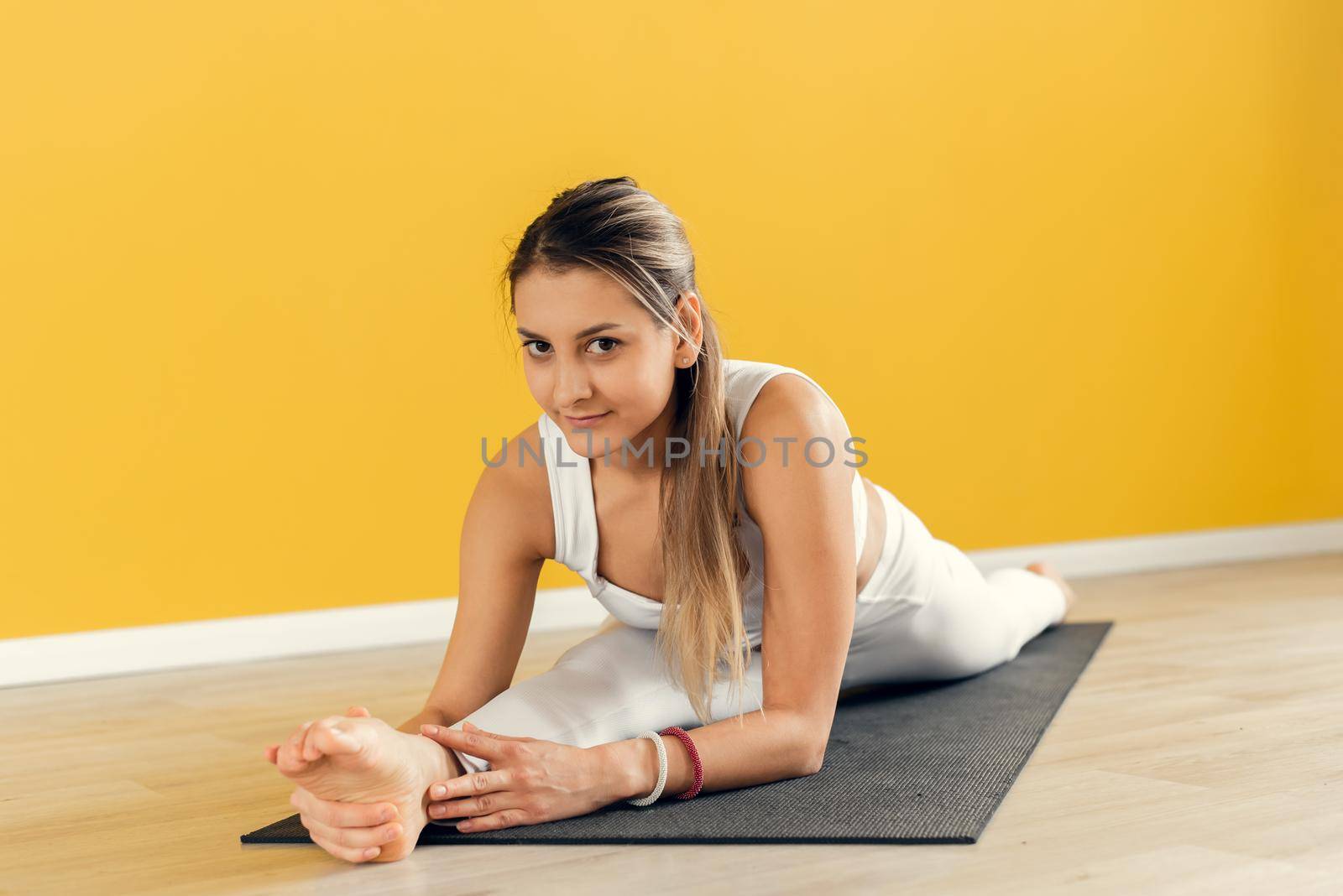 Sporty caucasian woman sitting in splits, doing legs stretch, improving flexibility. Athletic lady keeping fit and looking at camera.