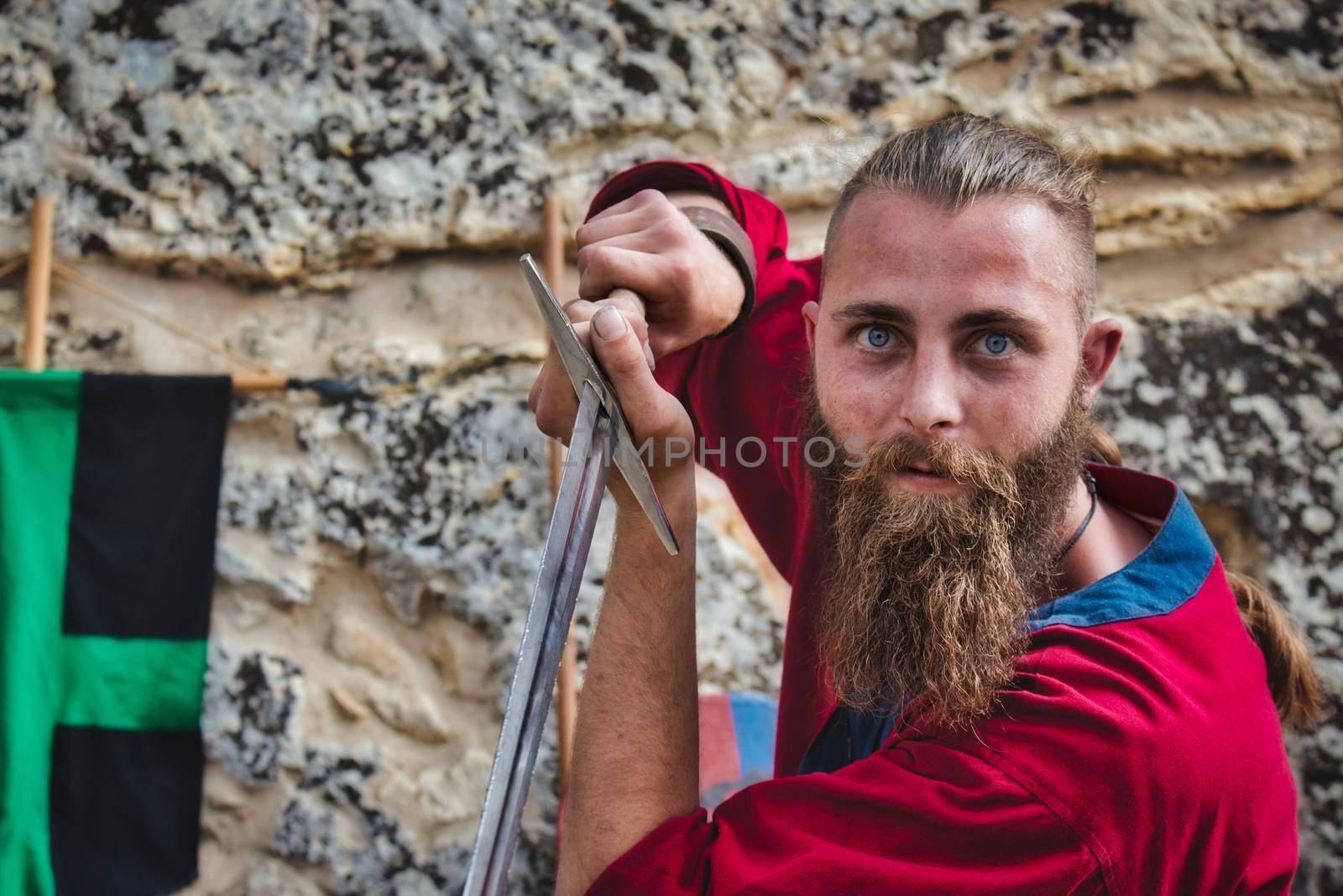 A bearded viking brandishing a steel broadsword looking at the camera