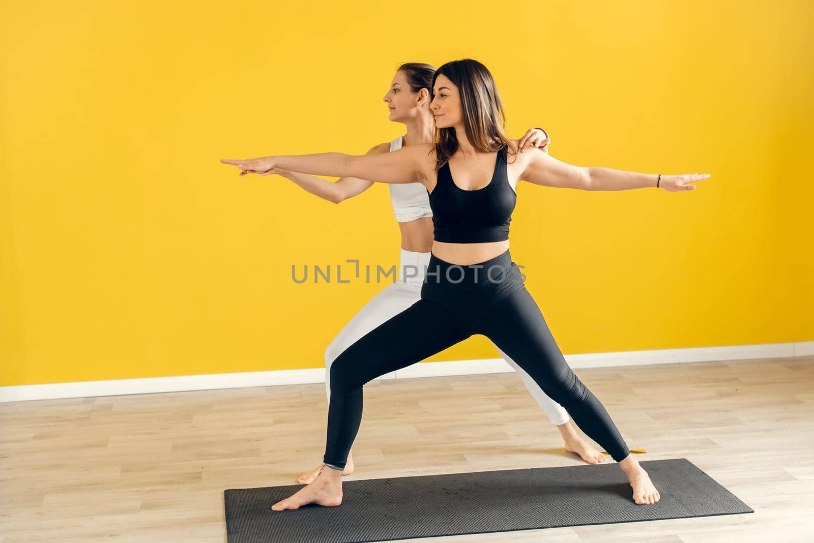 Fitness woman training with her personal trainer at gym. Young couple doing stretching exercises, Virabhadrasana, pose Warrior, copy space.