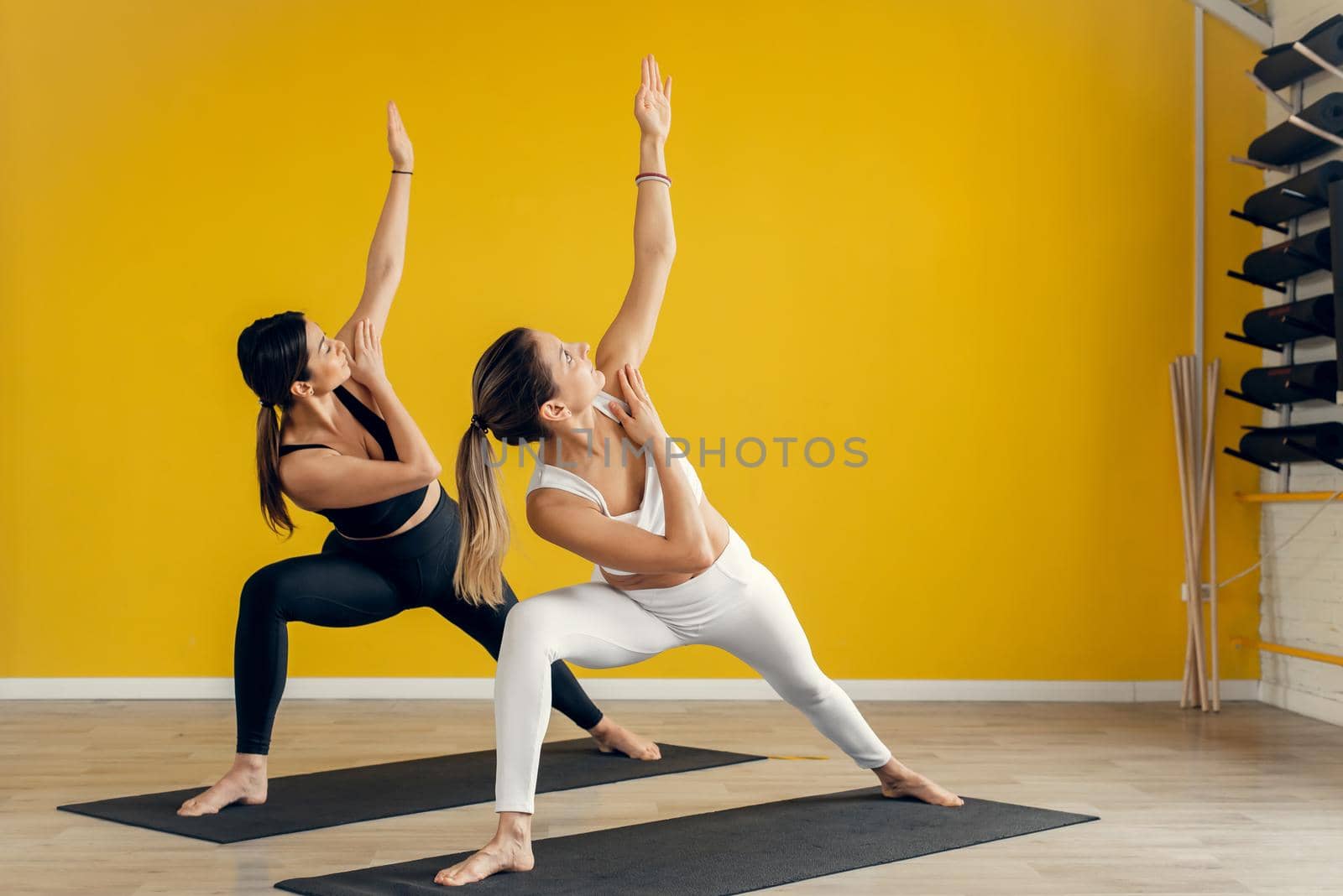 Two young women practicing yoga, doing exercises, training, female students train in a sports club, studio.