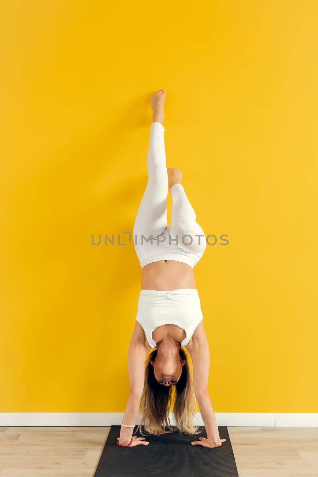 Yogini practicing yoga pose in the gym. The woman stands upside down.